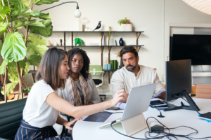 Three people of different backgrounds sit around a computer.